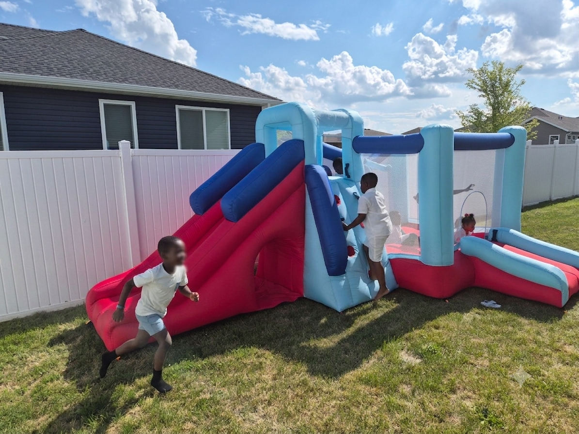 Kids playing on a red and blue inflatable bounce house with slide and climbing wall